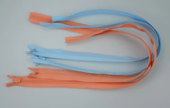 Two closed-end zippers, one light blue and one orange, arranged in loops on a plain white surface