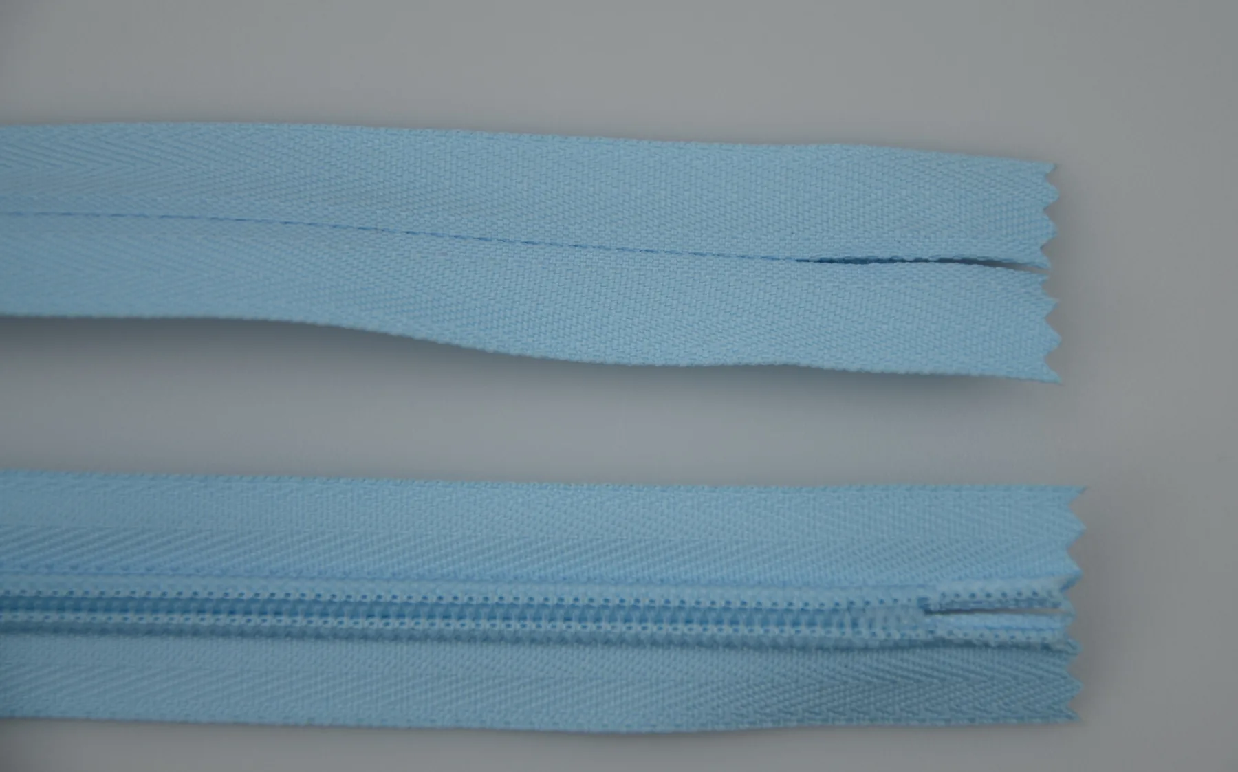 Two lengths of light blue nylon zipper tape on a plain gray background, one showing the coil teeth