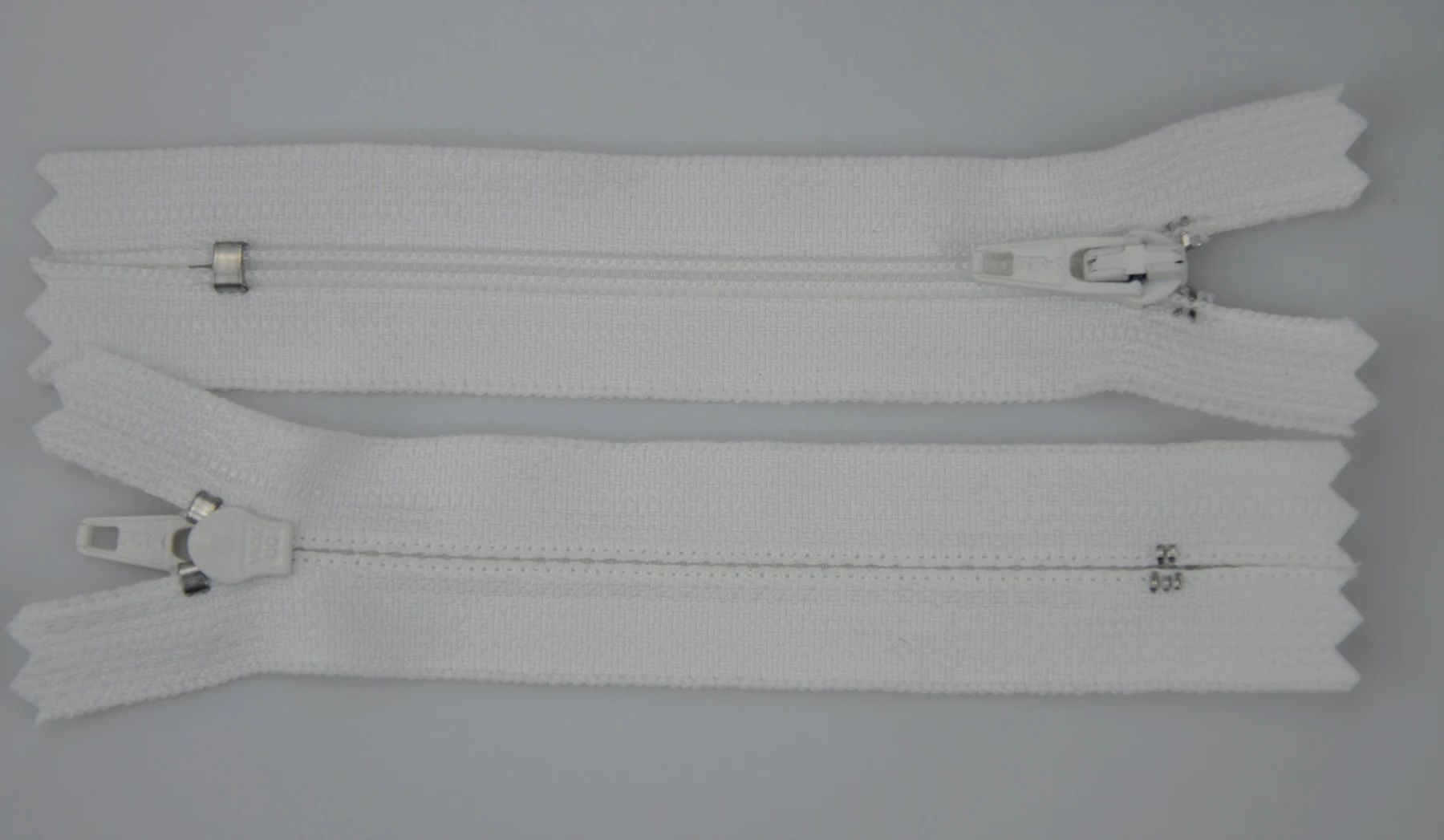Two white zippers with metal sliders lying parallel on a plain light gray background
