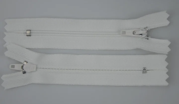 Two white zippers with metal sliders lying parallel on a plain light gray background