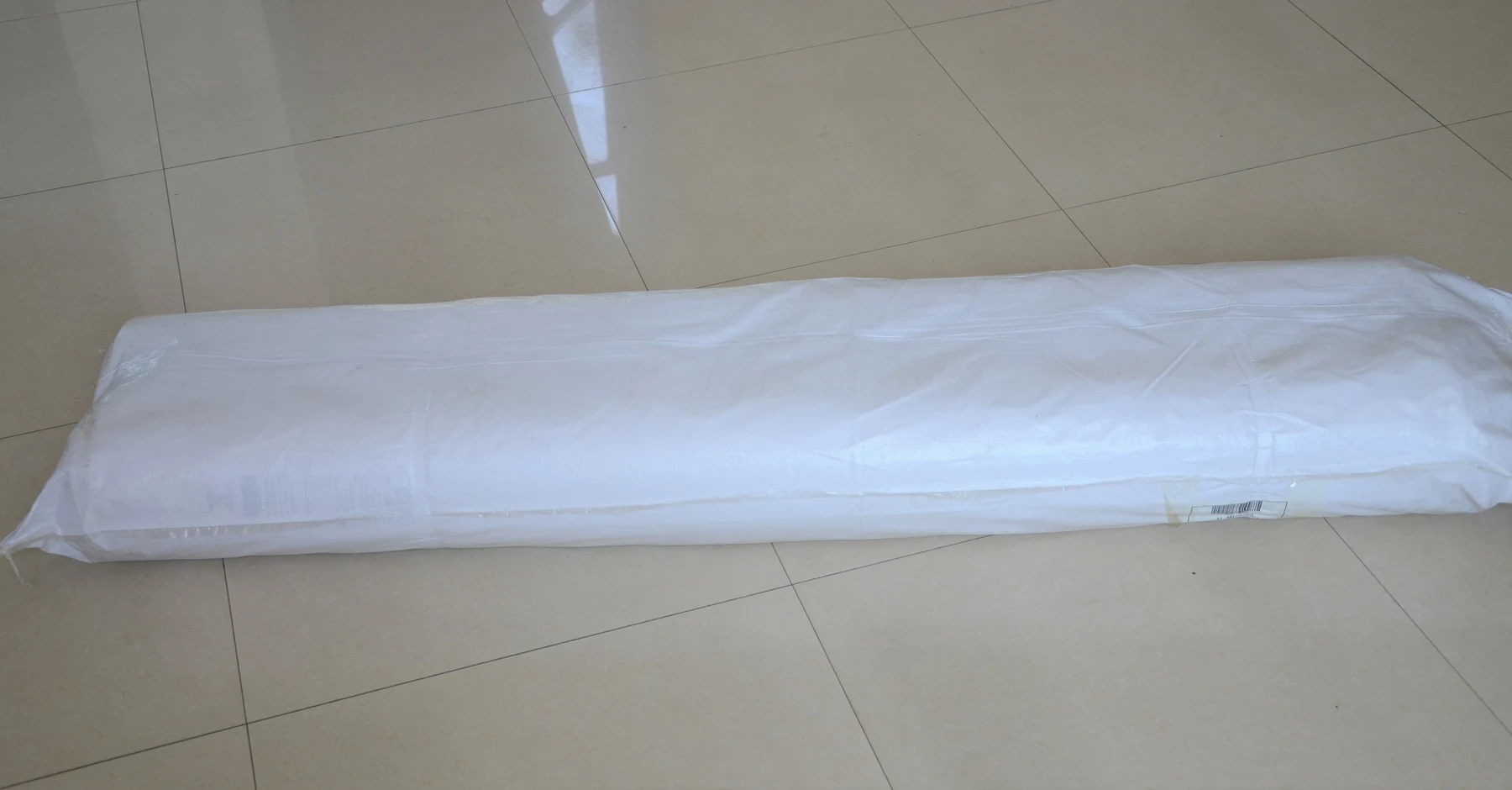 Long object wrapped in white plastic lying on a beige tiled floor