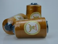 Three golden MUSATEX 100% polyester sewing thread cones with branded paper labels on a plain light background