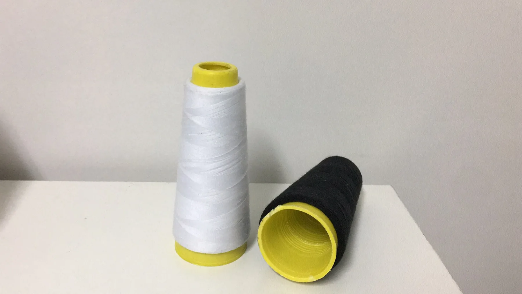 Two polyester thread cones, one white standing upright and one black lying on its side, on a white surface