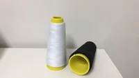 Two polyester thread cones, one white standing upright and one black lying on its side, on a white surface