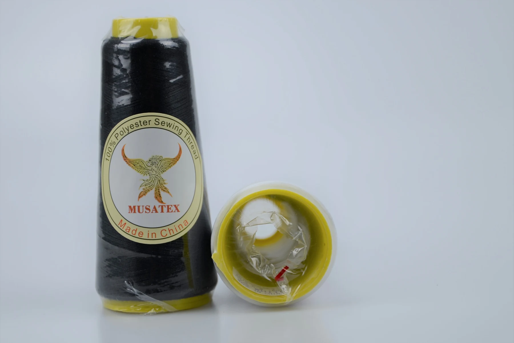Two black polyester sewing thread cones with yellow ends, one showing a MUSATEX phoenix label, on a plain light background.