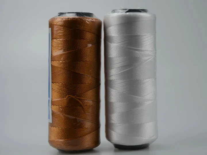 Two large spools of industrial thread, one copper-brown and one white, wrapped in plastic on a plain background