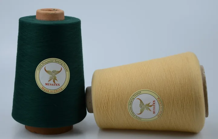 Two MUSATEX sewing thread cones, dark green upright and pale yellow lying down, on a light background