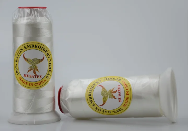 Two white rayon embroidery thread cones with MUSATEX phoenix labels on a light background