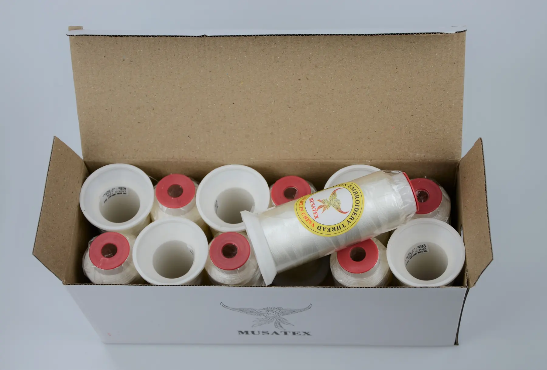 Open carton of MUSATEX branded spools of white thread.