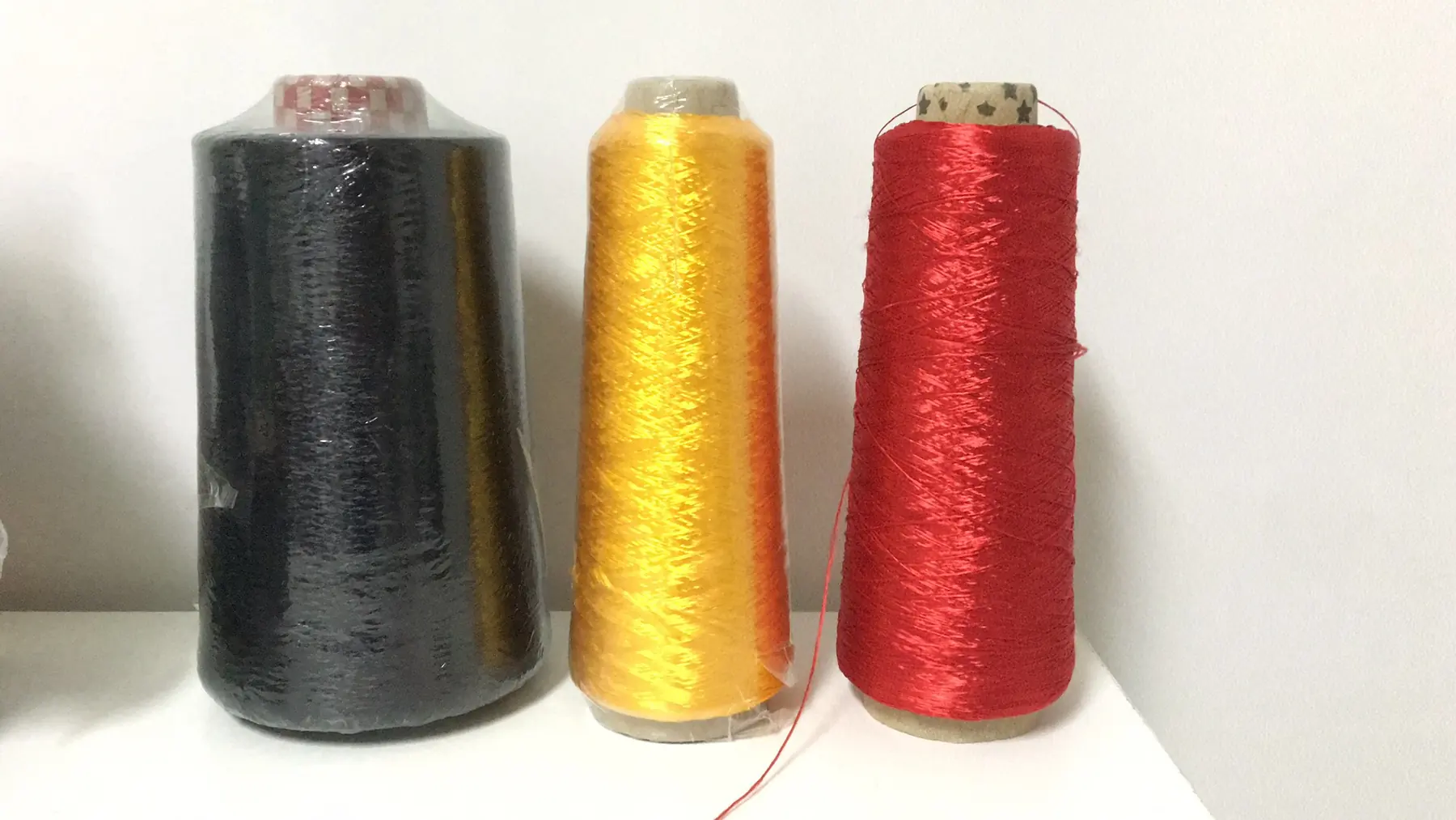 Three large spools of thread in black, gold, and red on a white surface against a plain wall