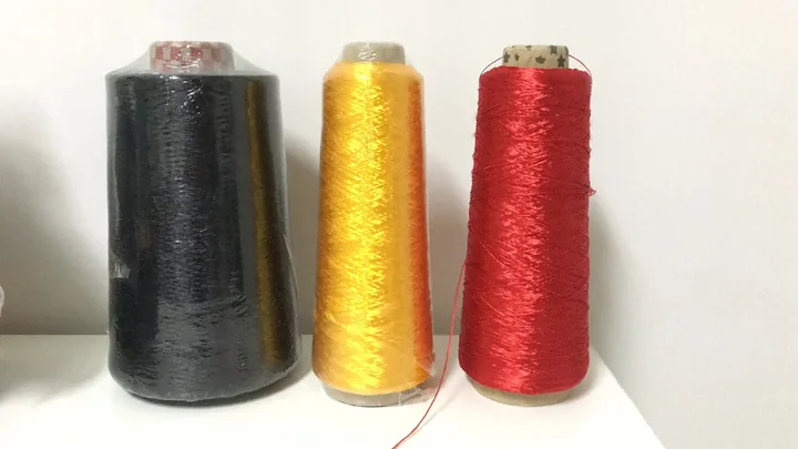 Three large spools of thread in black, gold, and red on a white surface against a plain wall