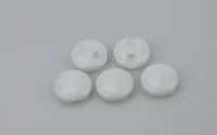 Five small white round ceramic or plastic discs with slotted tops arranged on a light gray background
