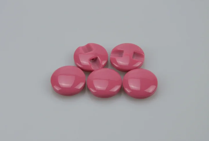 Five glossy pink round plastic buttons, two showing slot holes, arranged on a plain gray background