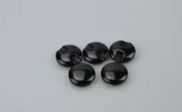 Five glossy black round plastic buttons or caps arranged on a plain white background