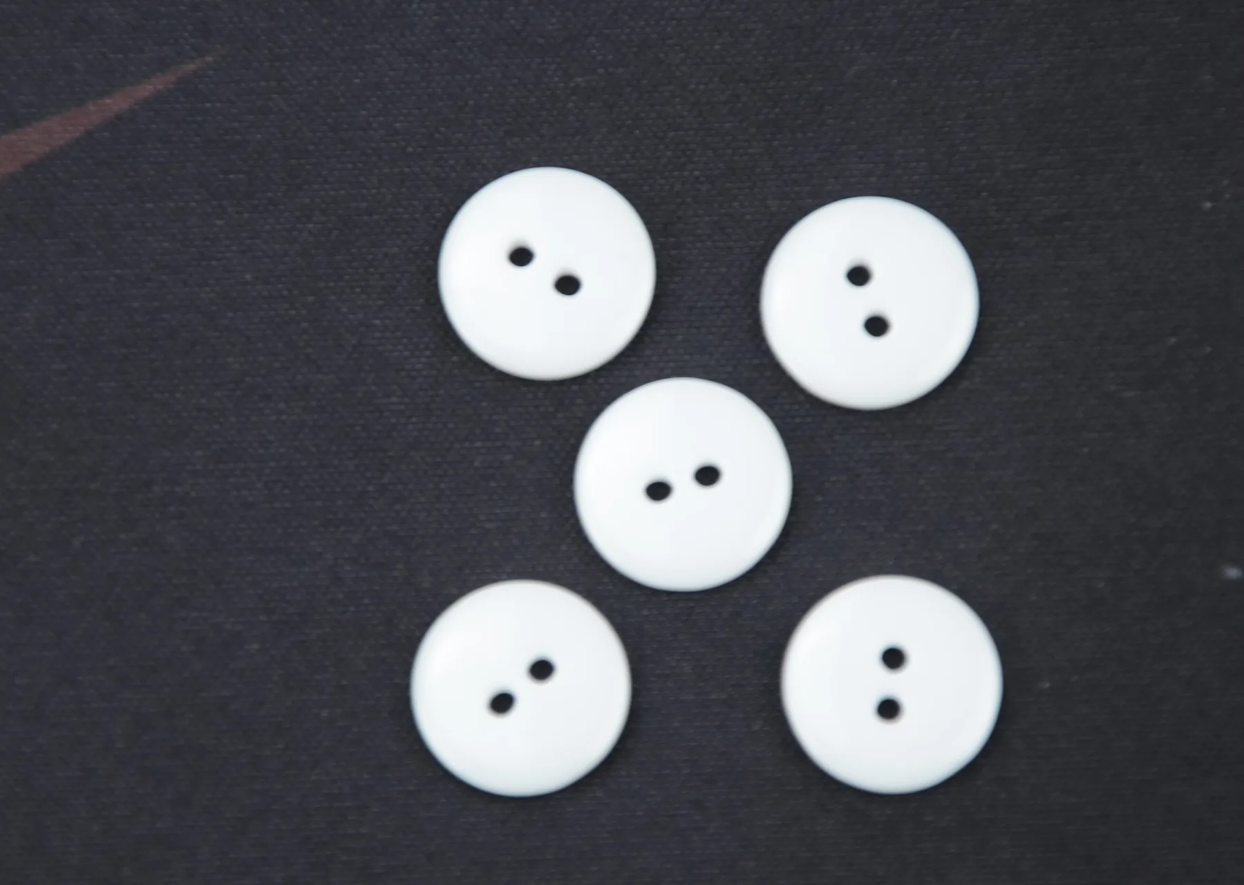 Five white two-hole round buttons arranged on a dark textured surface