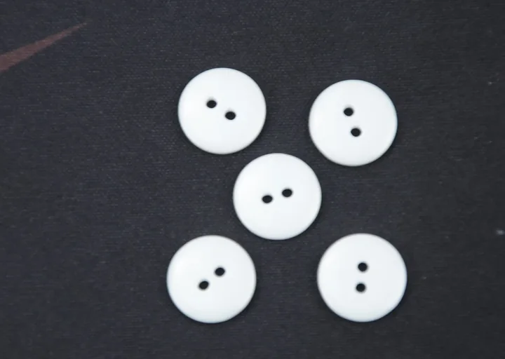 Five white two-hole round buttons arranged on a dark textured surface
