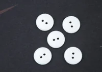 Five white two-hole round buttons arranged on a dark textured surface