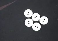 Five white two-hole buttons arranged on a dark gray fabric surface