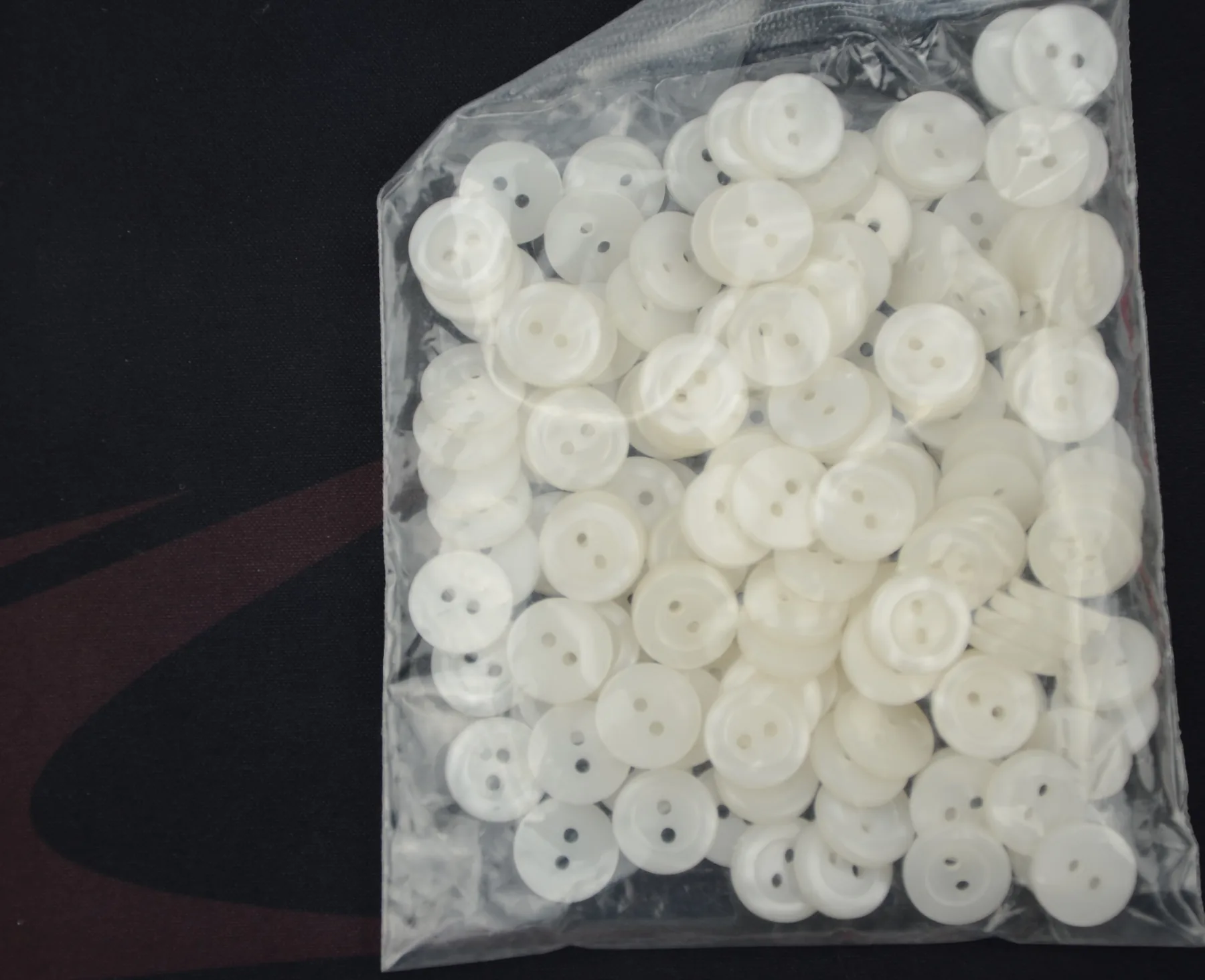 Clear plastic bag filled with small white two-hole buttons on a dark background
