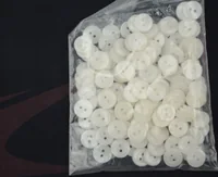 Clear plastic bag filled with small white two-hole buttons on a dark background