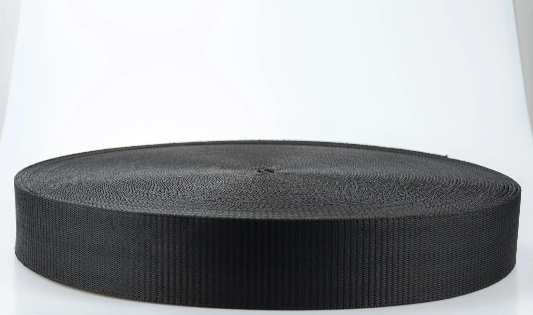Large roll of black woven webbing strap on a clean white background