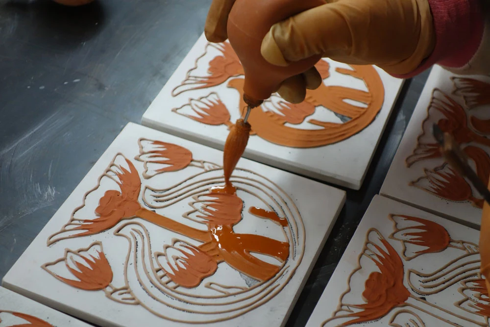 Artisan filling a tulip motif tile with terracotta coloured glaze by hand
