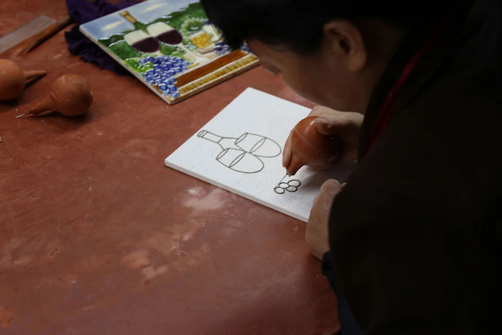Artisan drawing raised outlines on rectangular ceramic tiles