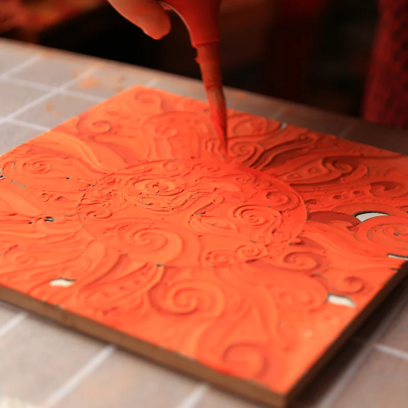 Close view of thick orange glaze filling the raised outlines of a tile