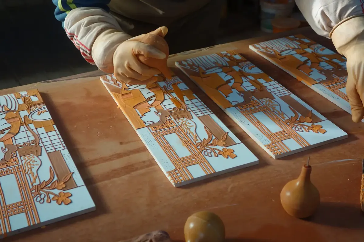 Workshop artisans raising clay outlines on ceramic tile blanks before glazing