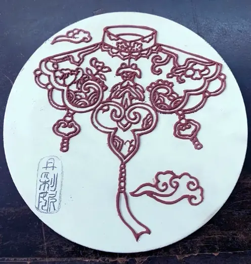Raised clay outlines applied by hand onto a round porcelain tile blank