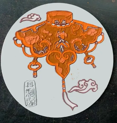 Round tile with orange and brown glazes filled inside the raised clay outlines