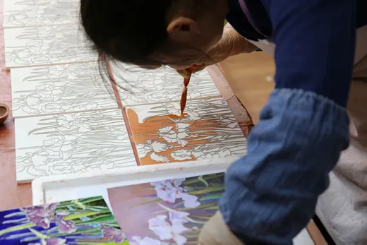 Painter filling iris motif tiles with coloured glaze at the workbench