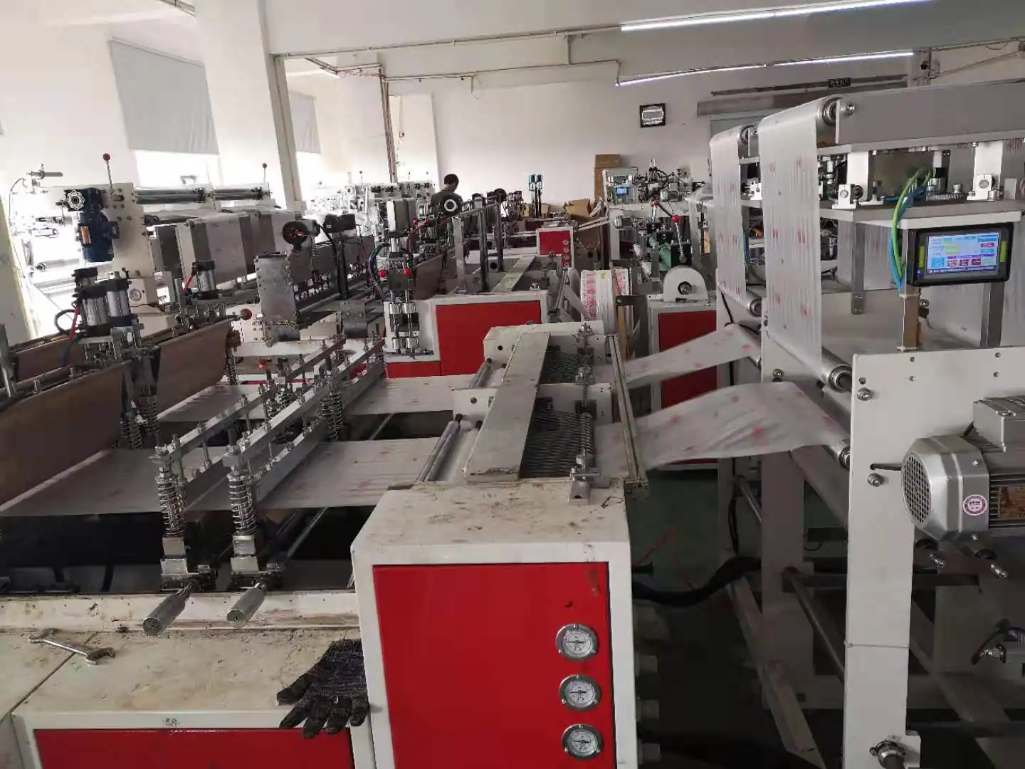 Interior view of a factory floor showing a long line of industrial machinery with red and white casings.