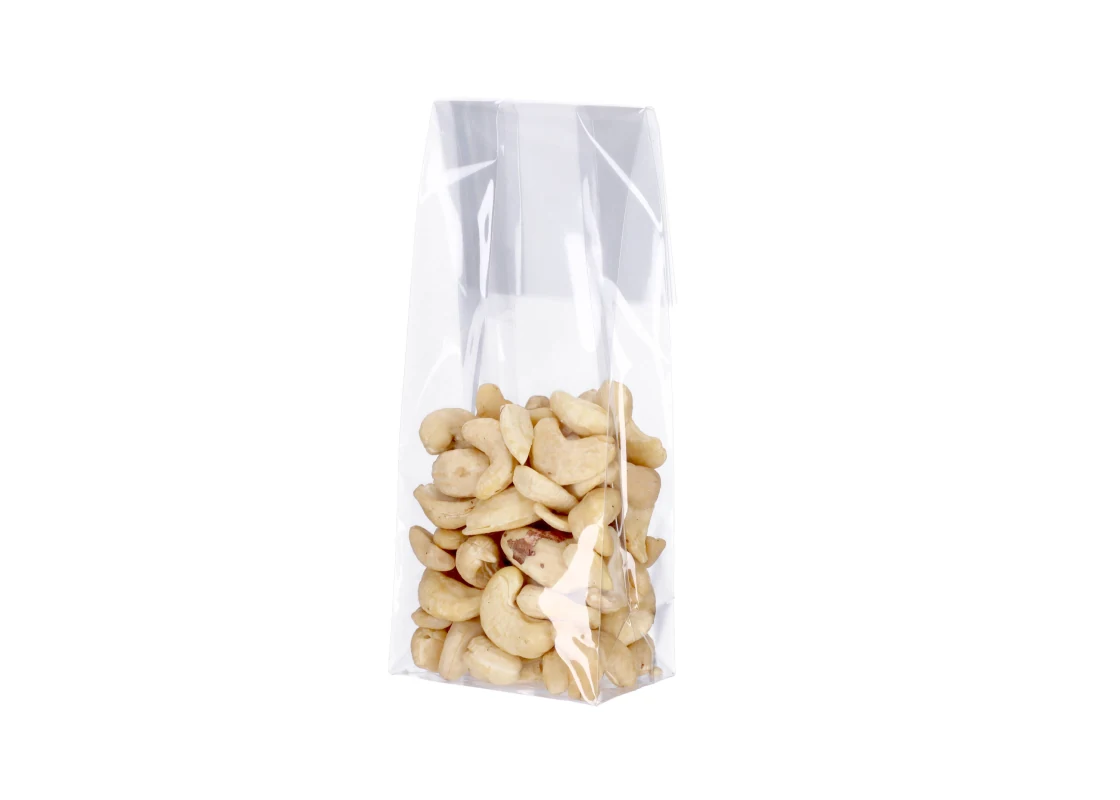 Clear cellophane bag filled with cashew nuts standing upright on a white background