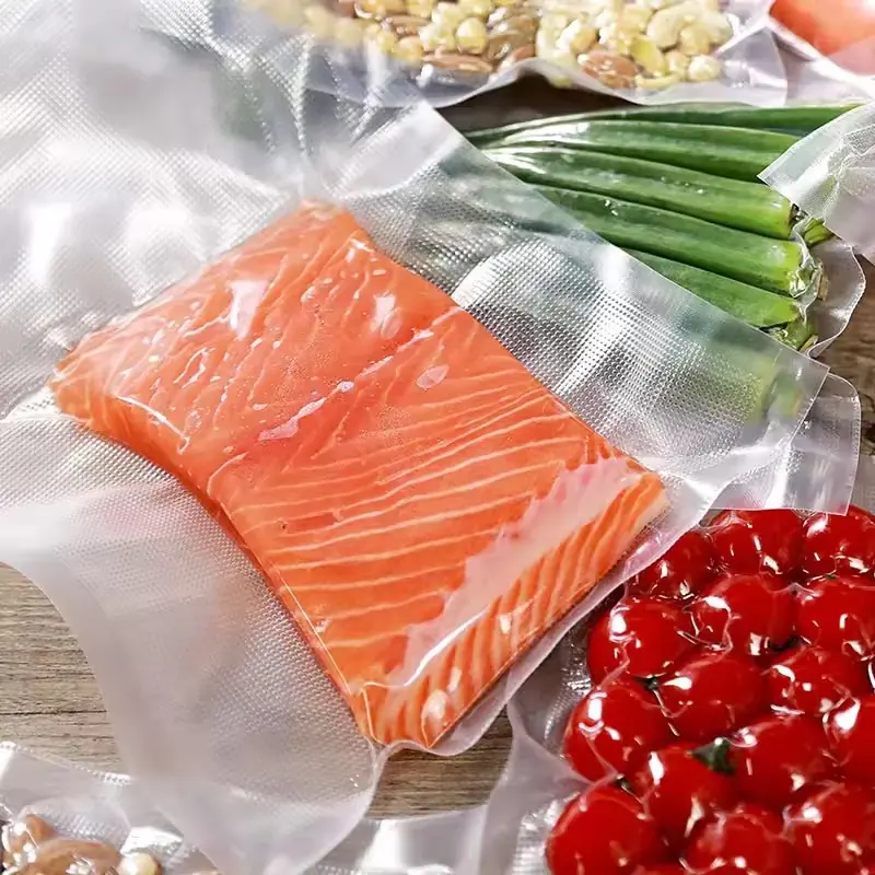 Raw salmon fillet vacuum-sealed in a textured plastic bag beside sealed bags of okra and cherry tomatoes