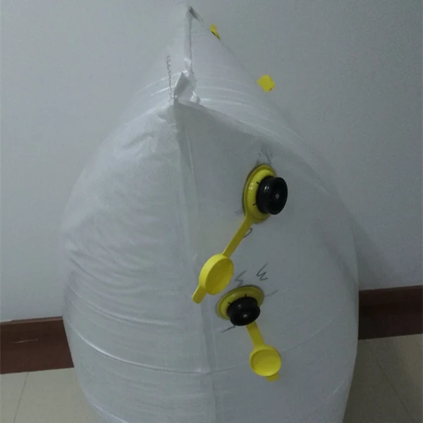 White FIBC bulk bag with yellow filling spouts and black caps, leaning against an indoor wall
