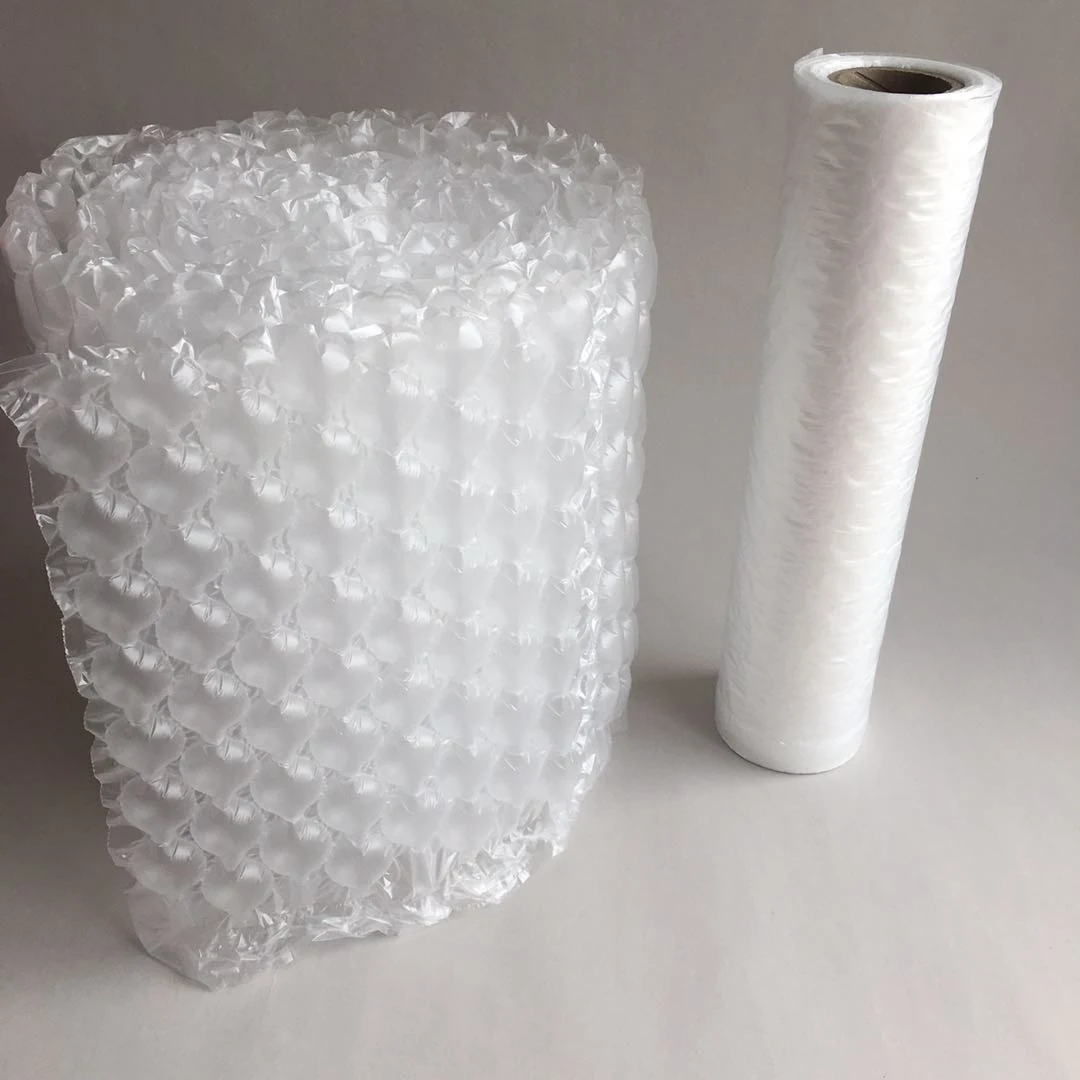 Large roll of clear bubble wrap standing beside a white foam packing roll on a plain gray background