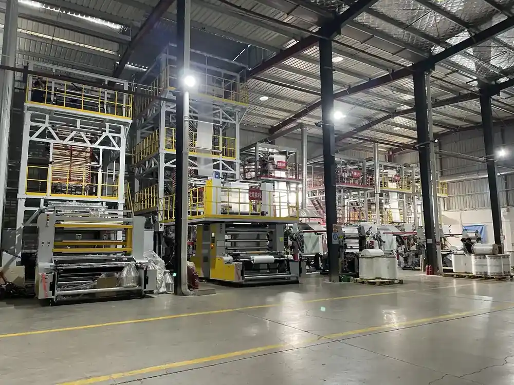 Interior of a large industrial factory featuring heavy machinery, yellow safety railings, and concrete floors
