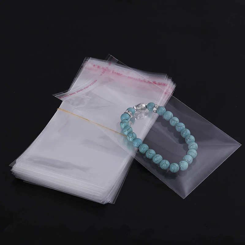 A stack of clear self-adhesive plastic bags with a blue beaded bracelet resting on top.