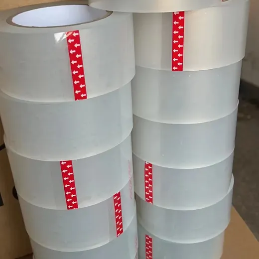 Stacks of clear BOPP packing tape rolls with red arrow-printed film inserts, packed in cardboard boxes