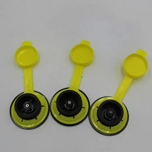 Three yellow plastic caps with flip-up lids and black valve assemblies arranged on a white surface