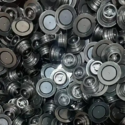 Bulk pile of black circular plastic diaphragm discs with ribbed and domed centers
