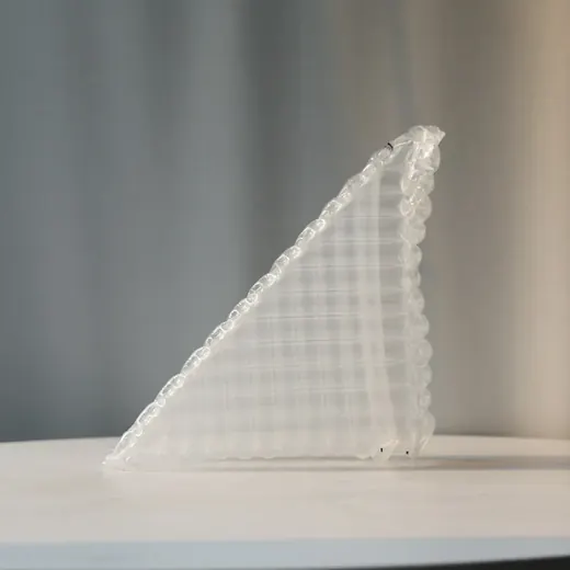 A transparent, triangular inflatable object standing upright on a white surface.