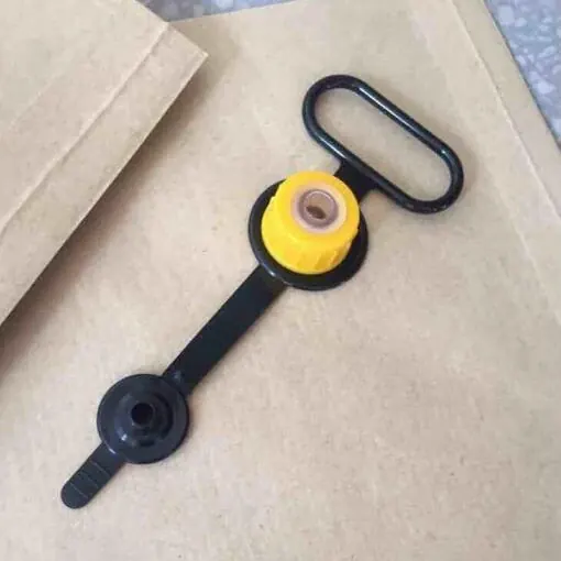 Yellow plastic drum cap with black pull handle and wrench strap lying on a beige surface