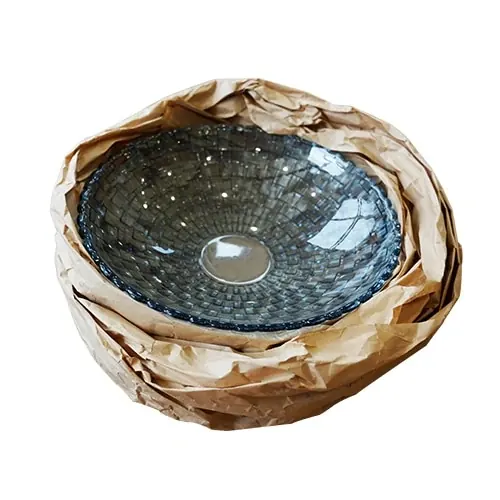 Grey mosaic-textured glass bowl nested in crumpled brown packing paper on a white background