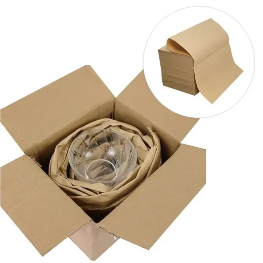 Cardboard box with brown kraft paper cushioning a glass bowl, beside a stack of packaging paper