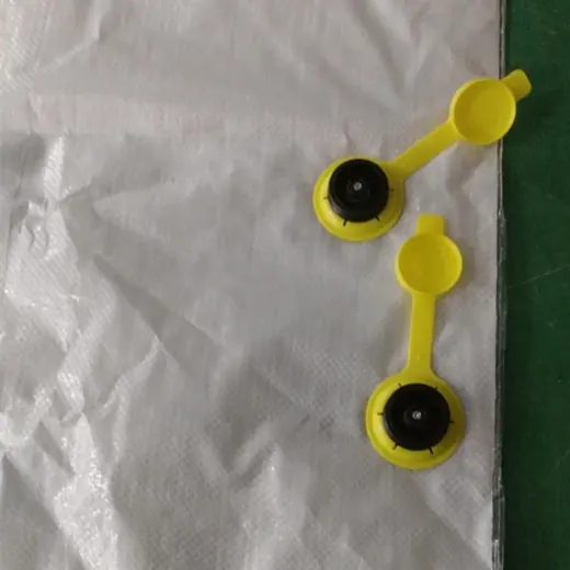 Two yellow plastic flip-top caps with black rubber seals placed on white woven fabric