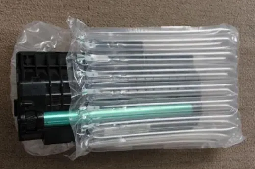 Printer cartridge with teal roller partially wrapped in air cushion packaging on carpeted floor