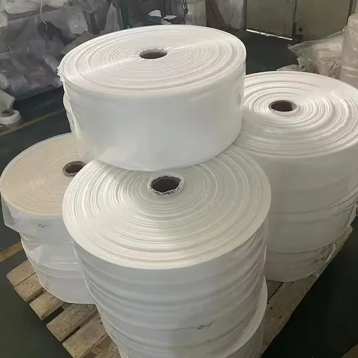 Large rolls of white plastic film stacked on a wooden pallet in a warehouse
