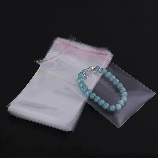 A stack of clear self-adhesive plastic bags with a blue beaded bracelet resting on top.